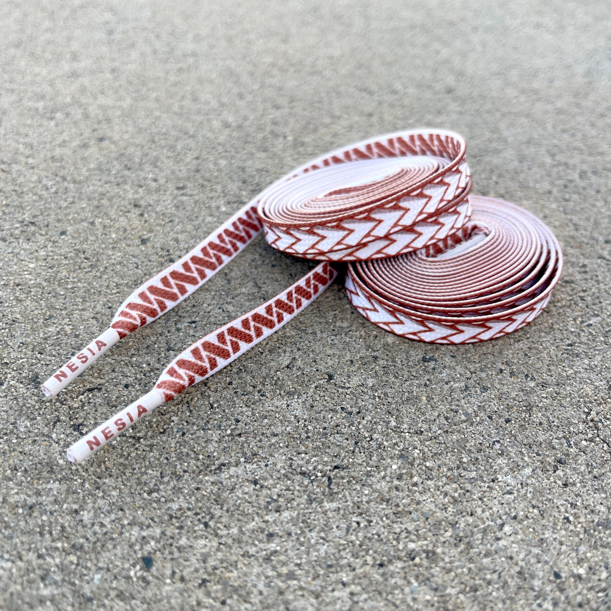 white nesia shoelaces with brown spear pattern rolled up on cement background