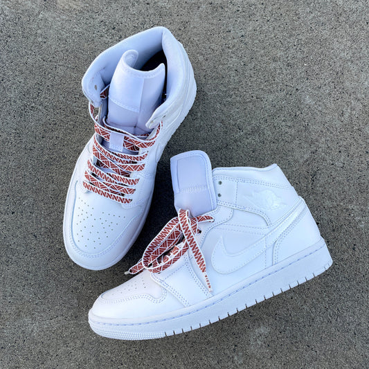 White Jordan 1 sneakers on a cement background with white and brown Nesia Originals shoelaces with a tapa pattern