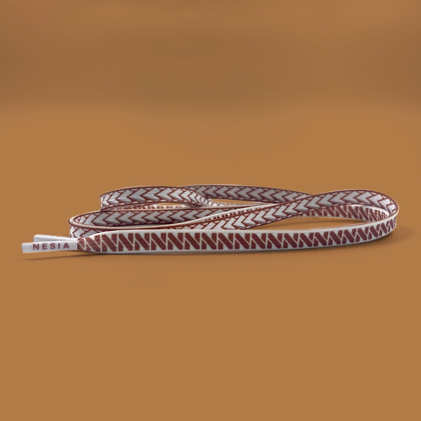 white nesia shoelaces with brown spear pattern on brown studio background