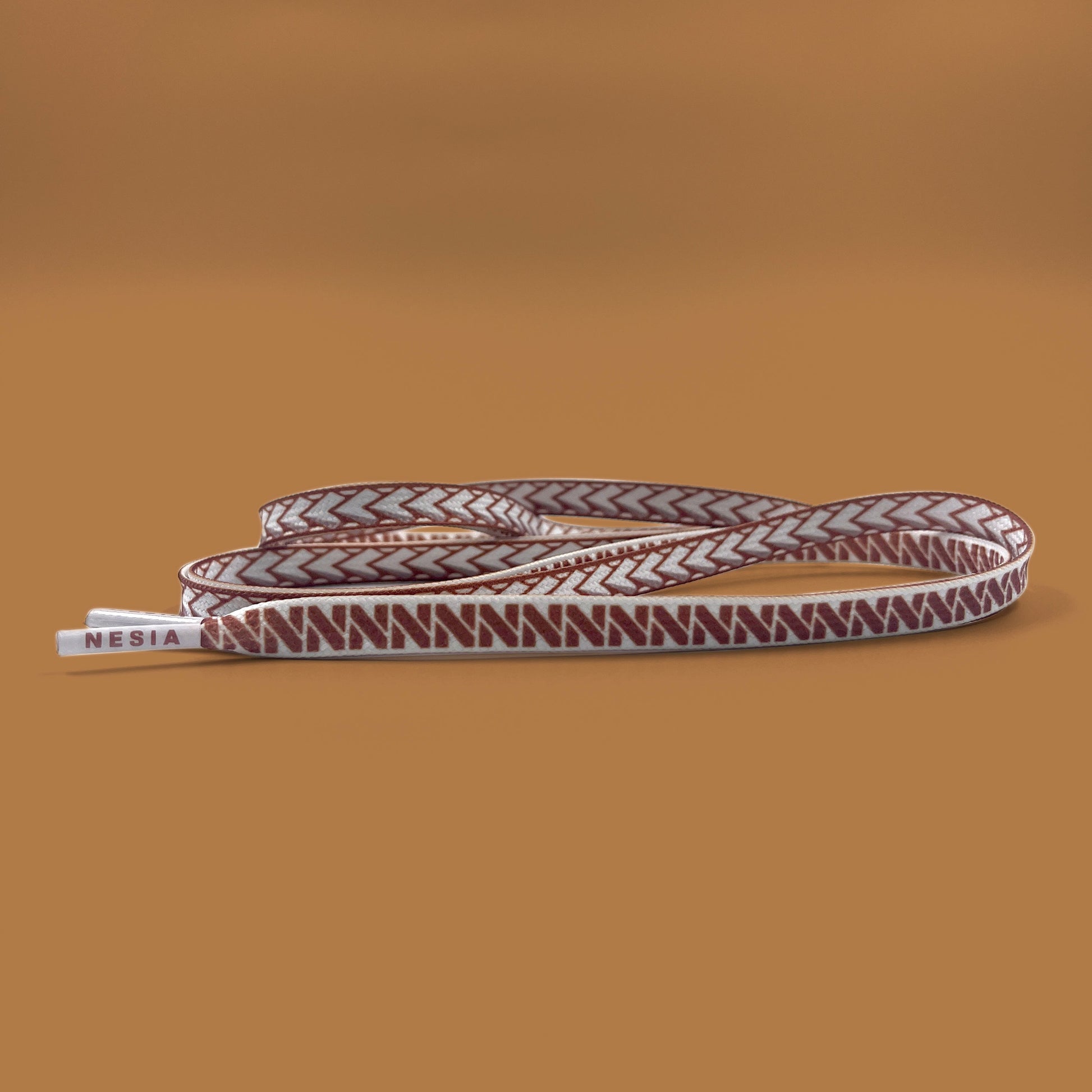 white nesia shoelaces with brown spear pattern on brown studio background